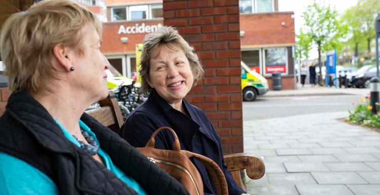 Two women sitting on a bench outside hospital talking