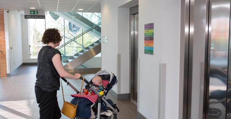 Woman pushing a push chair and waiting for a lift in a hospital 