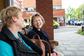 Two women sitting on a bench outside hospital talking